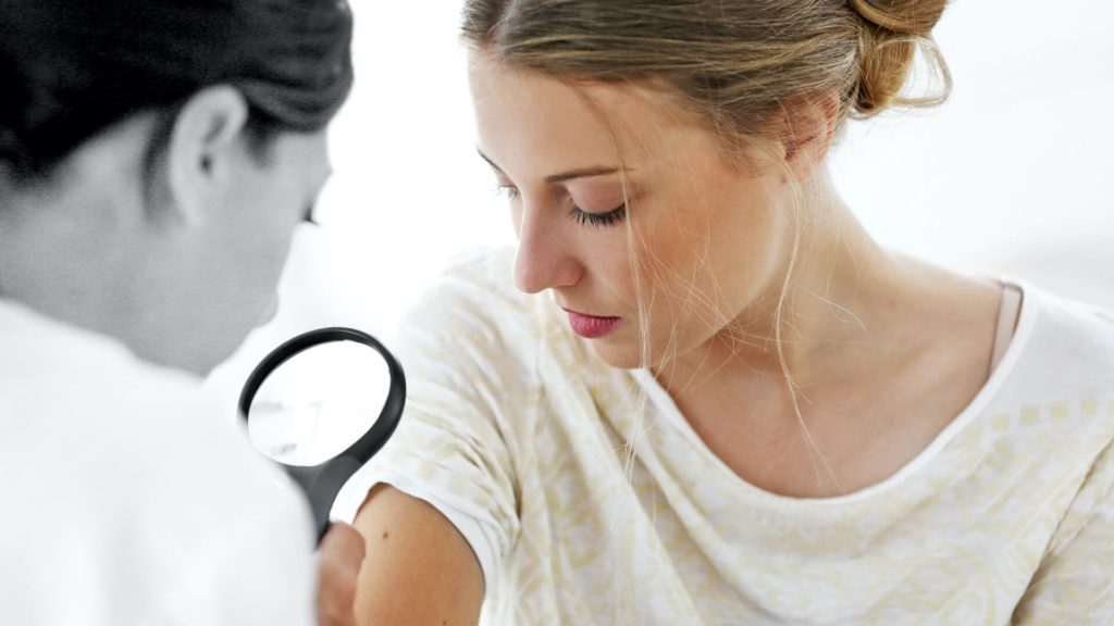 Eine Ärztin untersucht einen Leberfleck auf dem Oberarm einer Frau